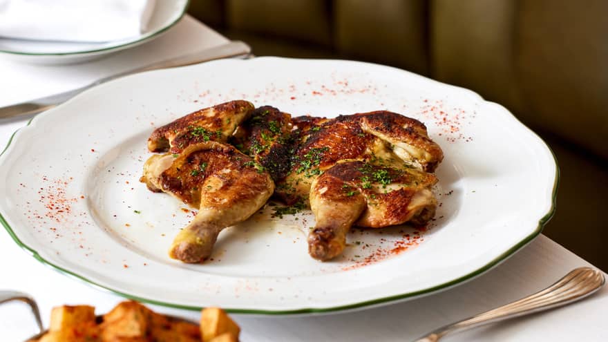 A roasted chicken dished served on a scalloped white plate with potatoes