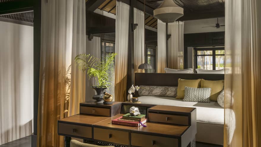 Interior of a private villa at a resort, with sheer curtains outlining a four-post king bed, and a wooden table at the foot of the bed