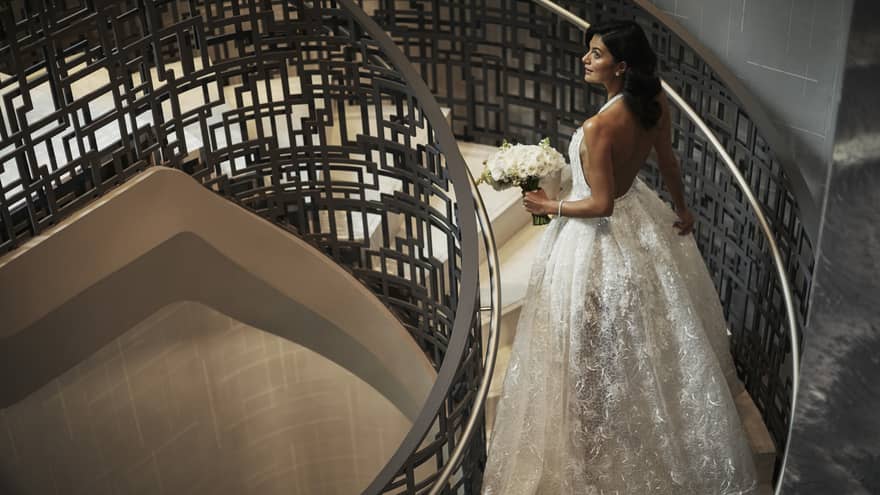 Bride wearing long white wedding gown walks up spiral staircase