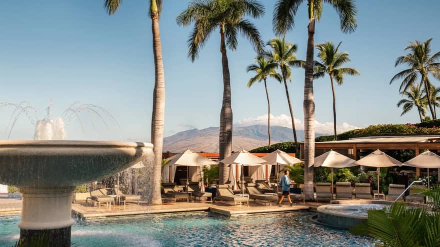 Pool with large fountain surrounded by palm trees and cabanas