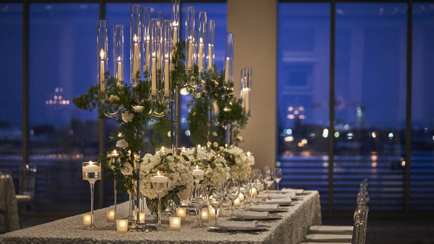 A long table with many tall candles and flowers along the center.