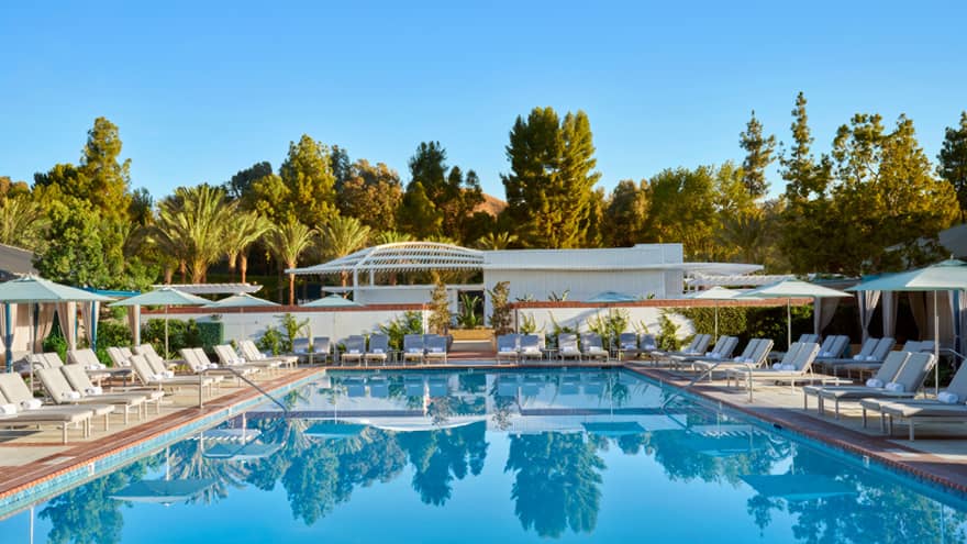 An outdoor pool surrounded by lounge chairs, umbrellas and trees.
