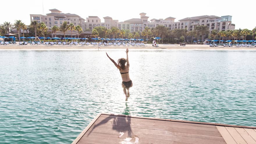 A woman jumps into a light blue lagoon.
