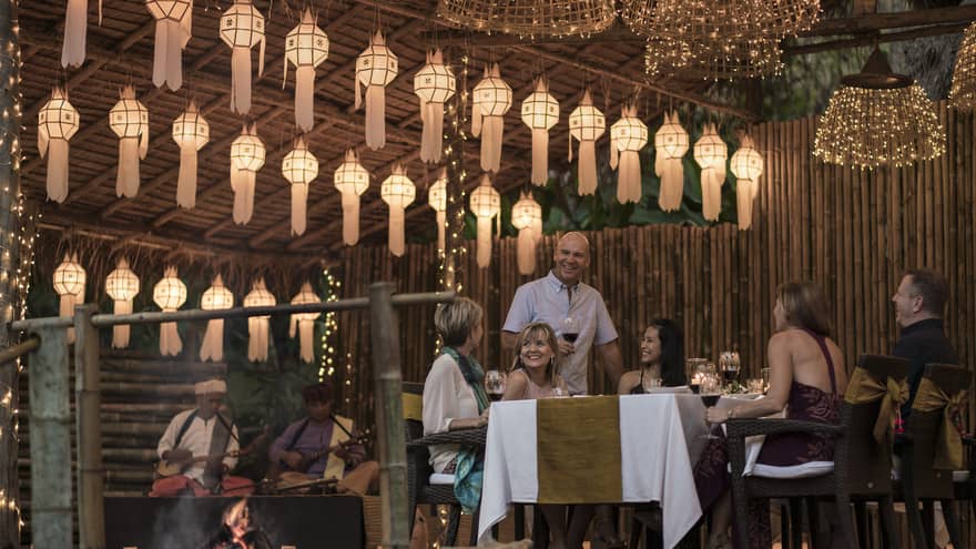 A group of people sitting at a table enjoying a meal in outdoor pavilion decorated with lanterns