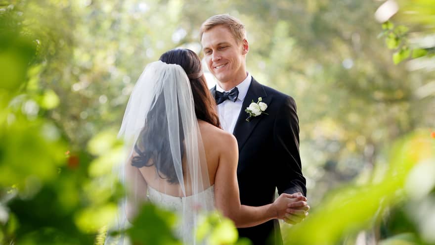 A person wearing a long veil dances joyfully with a smiling partner in a beautiful garden, surrounded by nature's splendor.
