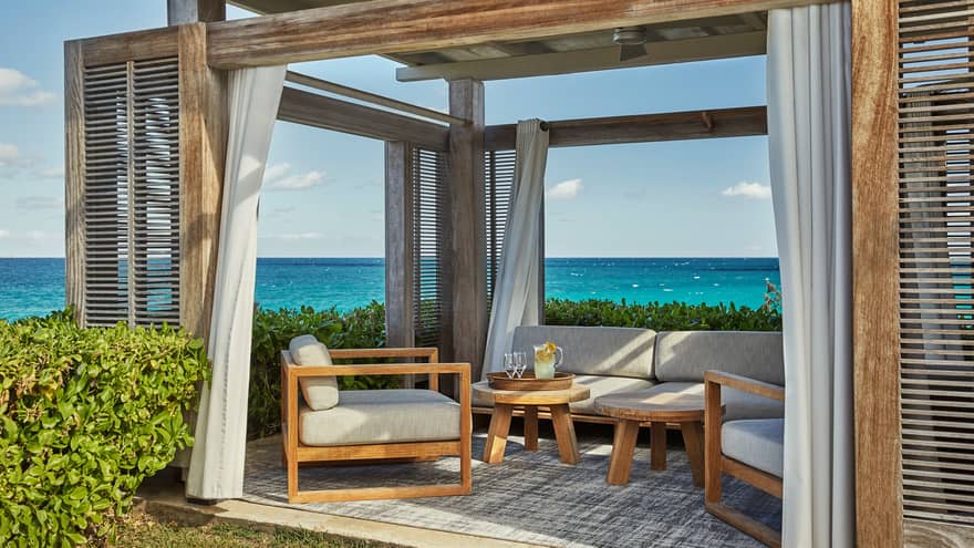 Patio chair and coffee table with jug of lemonade, glasses under pergola, blue ocean in background