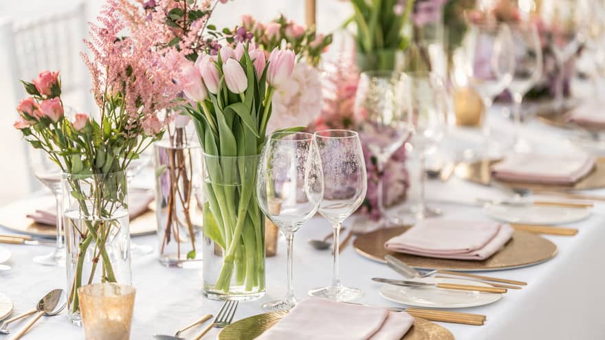 A banquet table is decorated with gold chargers, pale pink linens and a variety of pink florals