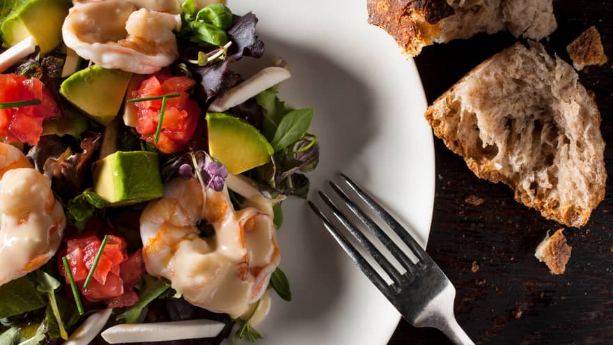 Fork on plate of steamed shrimp salad, greens 