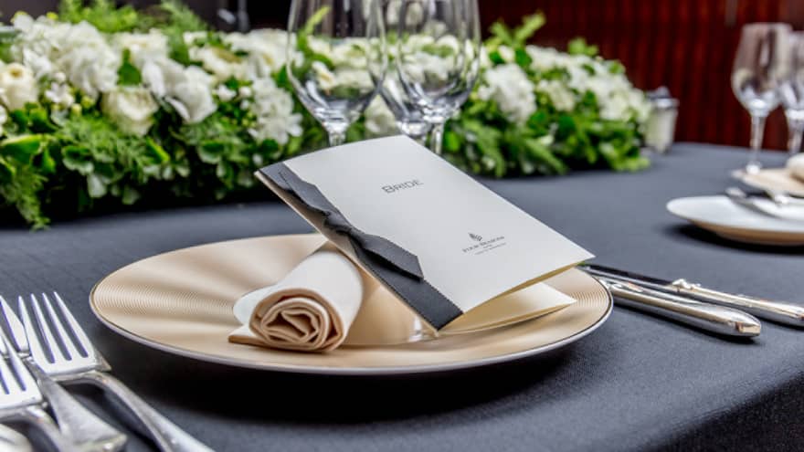 A wedding dinner table showcasing a crisp rolled napkin, elegant cutlery, floral arrangements and a stylish small booklet.