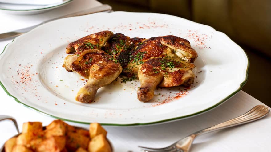 A roasted chicken dished served on a scalloped white plate with potatoes