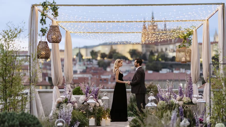 Couple in formalwear holding hands while facing each other on romantically decorated rooftop terrace