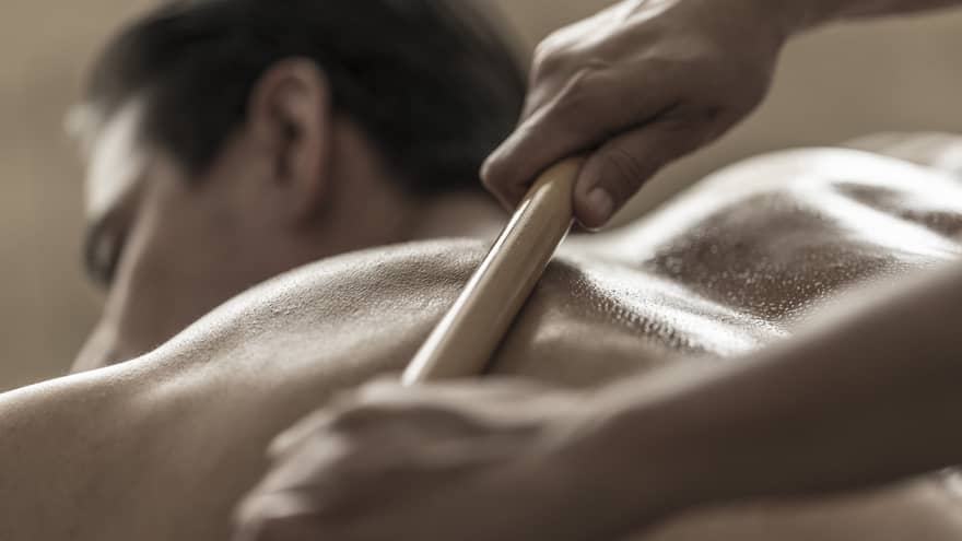 A spa attendant uses a tool to massage a guest's back
