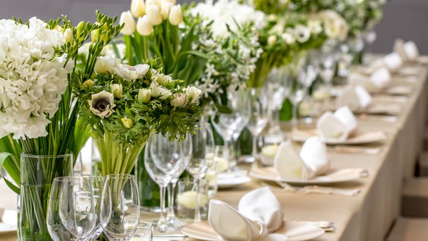 Close-up of long wedding dining table with wine glasses, white flowers in vases 