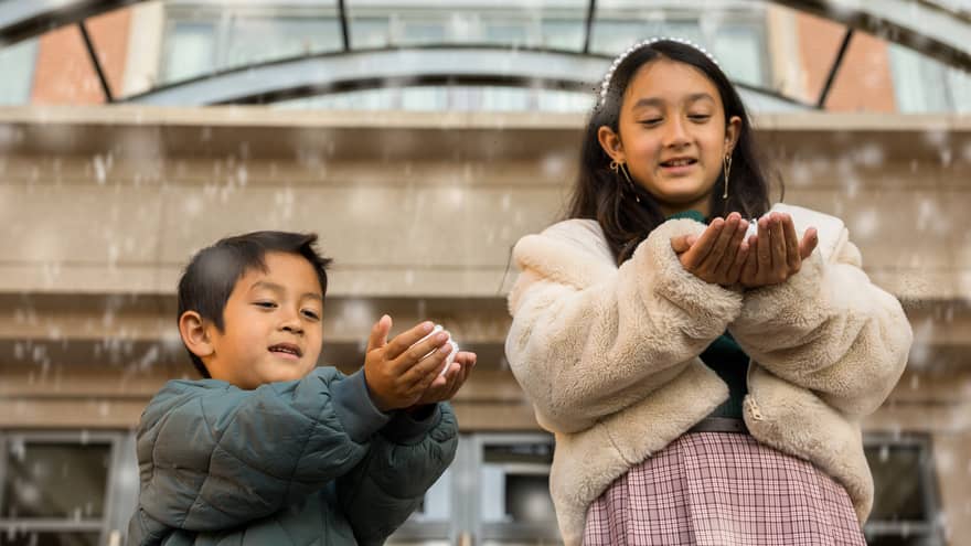 Two kids play with faux snow falling from the ceiling of a hotel entrance