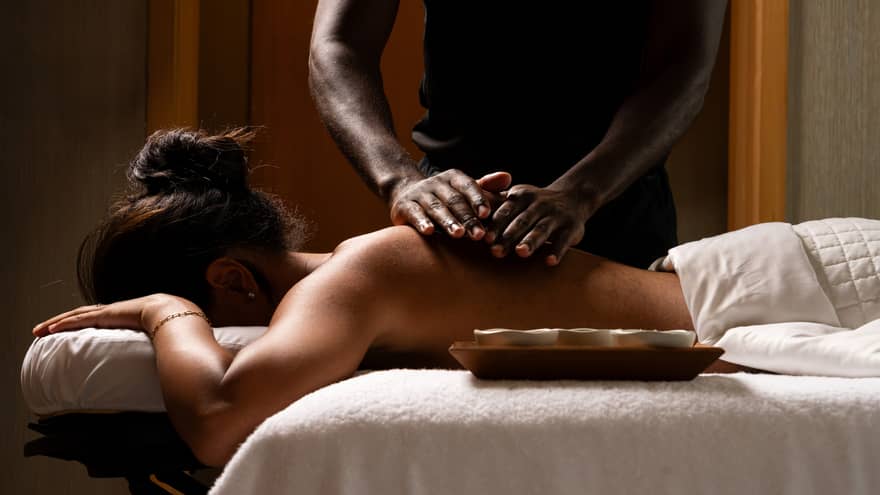 Masseur's hands rub oils on the bare back of a guest lying face down on a massage table