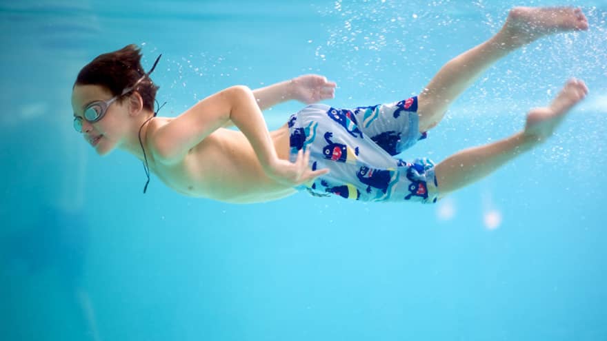 Underwater shot of a boy swimming in a pool with goggles and swim trunks