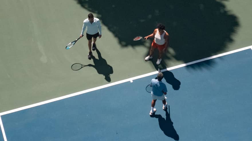 Three people holding tennis racquets on a tennis court.