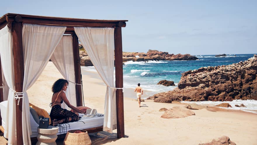 A woman on a small bed with a covering on a beach.