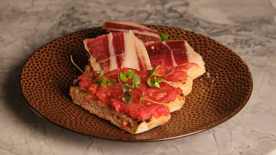 Pan con tomate served with sliced jamon on a brown stoneware plate