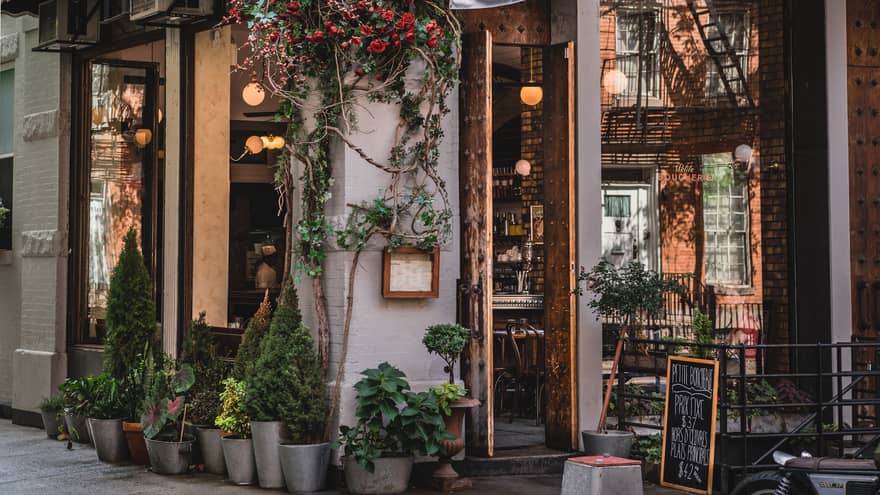 Outside of a restaurant with greenery and flowers at the entrance.