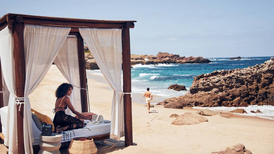A woman on a small bed with a covering on a beach.