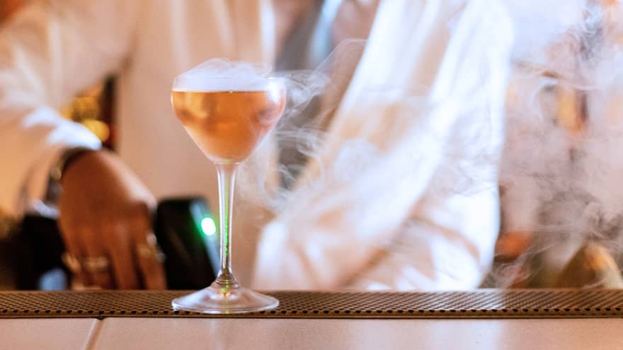 A bartender making a drink with a smoke garnish.