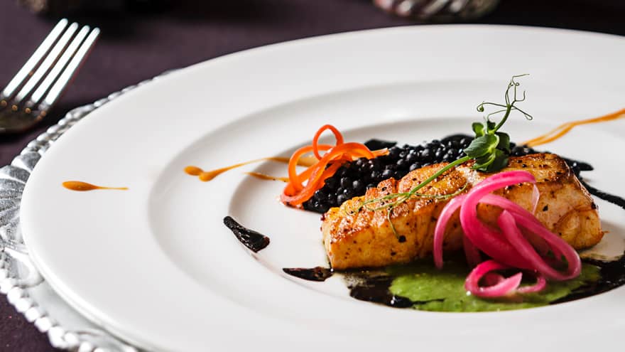 Baked Branzino fish fillet with pickled vegetable garnish, sauce on plate