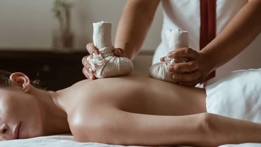 A woman being massaged by heavy stones in cloth bags.