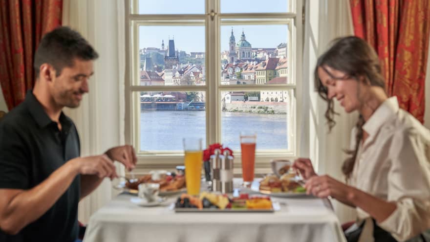 Man and woman eat breakfast at table, window looks out to Prague Castle