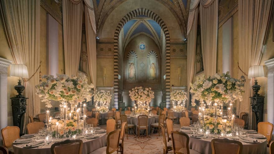 Grand dining room with tall arched ceilings and round elegantly set tables with tall white flower centrepieces