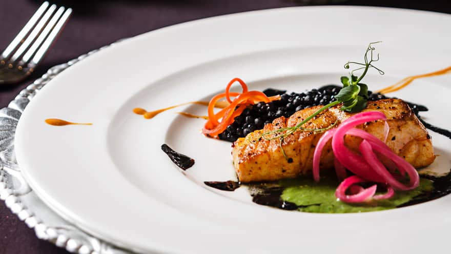 Baked Branzino fish fillet with pickled vegetable garnish, sauce on plate