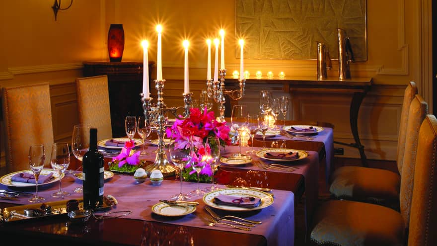 Elegant formal dining table with purple tablecloths, large silver candelabras with glowing candles, gold patterned chairs