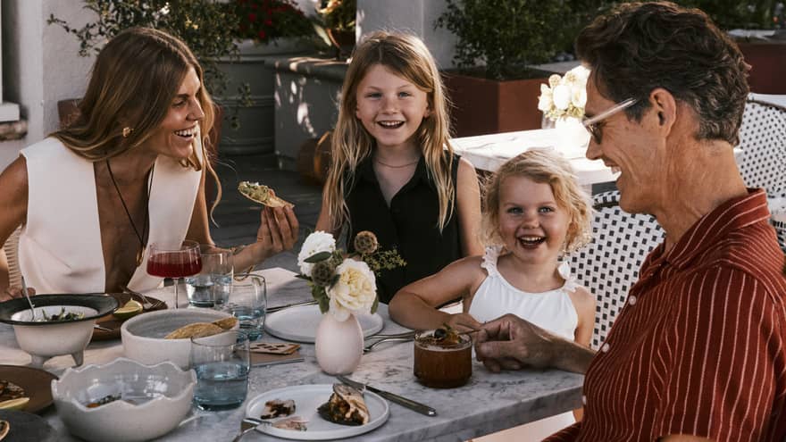 A family dining on a patio surrounded by trees and white columns