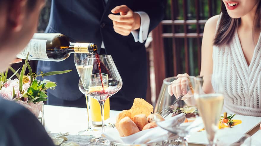 Server pouring red wine into large glass as couple dines at table