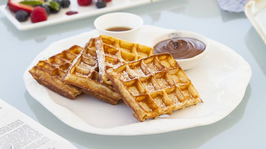Breakfast table with coffee cup, three waffles, fruit on plate