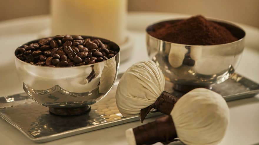 Two silver bowls on tray hold roasted coffee beans, ground coffee powder