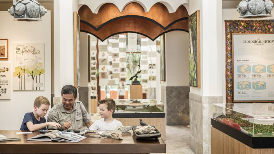 A man and two kids reading a book together at the Mangroves Discovery Centre at Four Seasons Langkawi