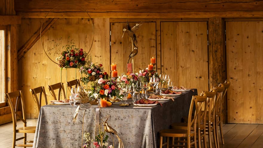 Dining table set with colourful floral centrepiece under vaulted wooden ceiling
