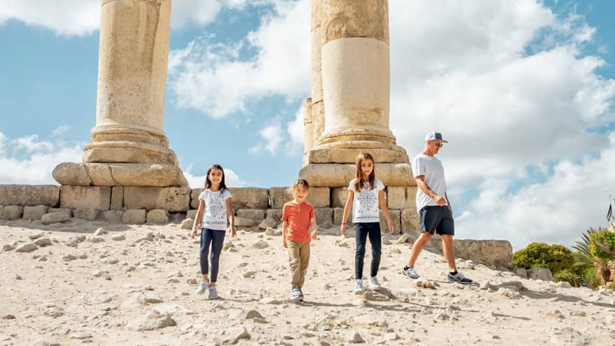 A parent and three children walk together next to the ruins of the Amman Citadel