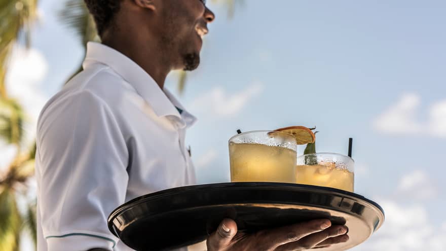 Smiling server carries tray with two cocktails, orange garnish