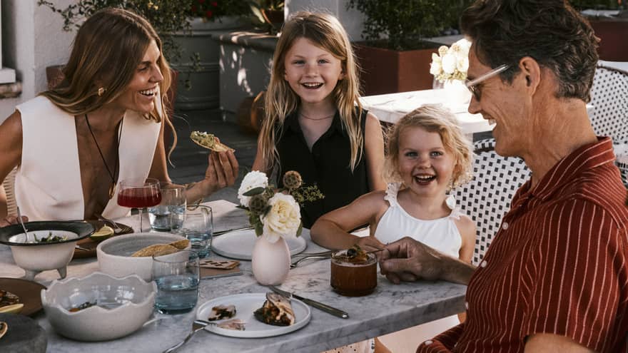 A family dining on a patio surrounded by trees and white columns
