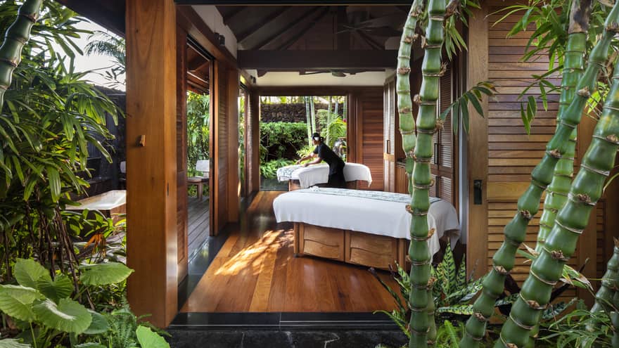 Spa staff spreads sheet on couples massage beds on open-air pavilion 