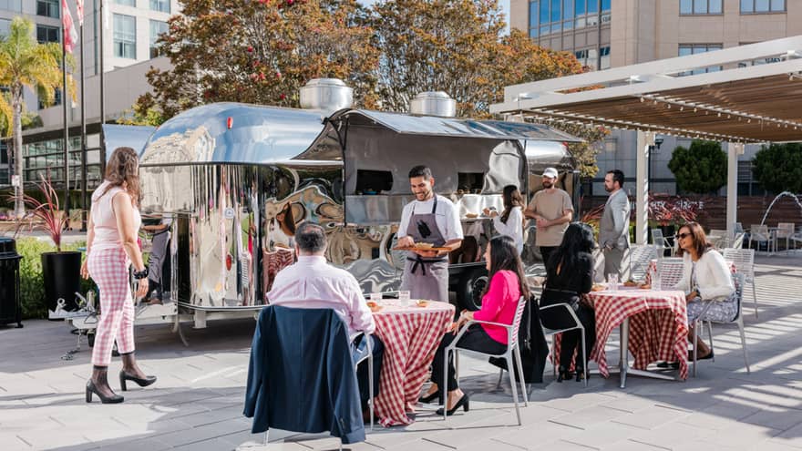 Outdoor venue with tables with red table cloths and the chef visiting a table.