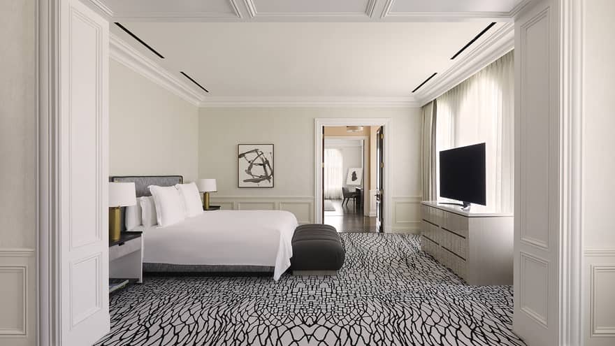 Bedroom with white and black carpeting, white king bed, black bench, TV and dresser