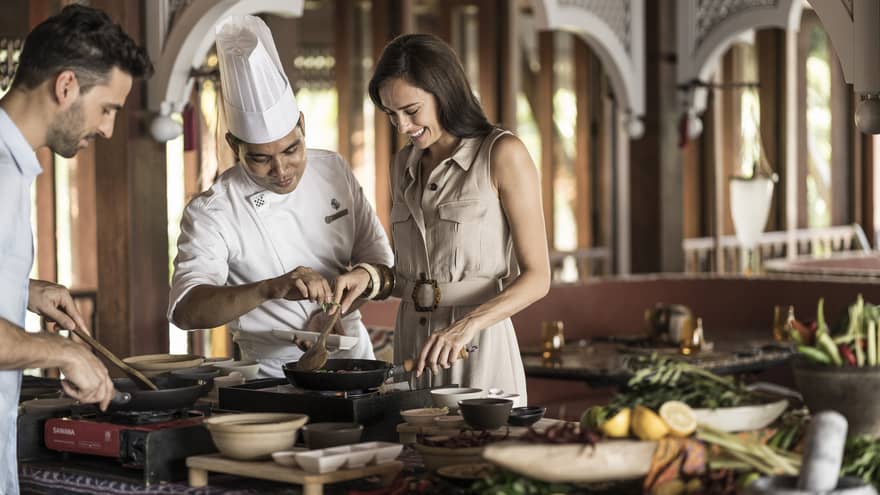 A chef doing an interactive cooking lesson with a man and a woman at the Four Seasons Langkawi