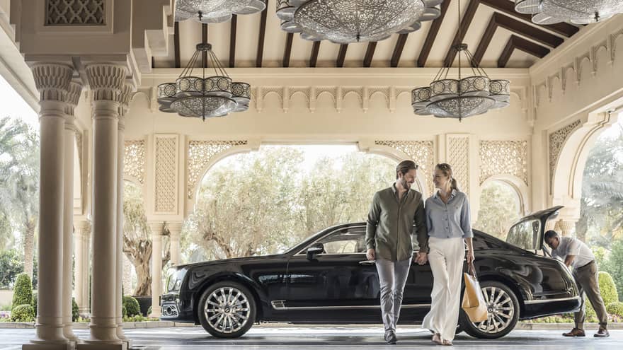 Couple holds hands, walks away from luxury car at entrance to Four Seasons Dubai at Jumeirah Beach