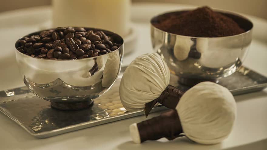 Two silver bowls on tray hold roasted coffee beans, ground coffee powder