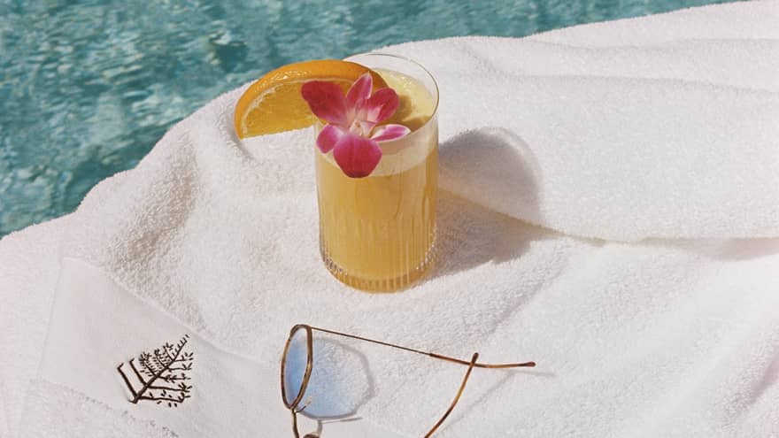 Tropical cocktail, sunglasses and a Four Seasons-branded bathrobe lay next to a pool