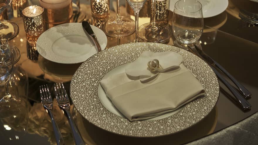 Wedding dining table place setting, napkin on plate, glassware and glowing candles in gold votives