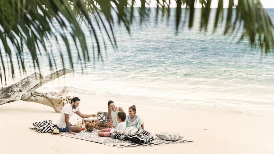 A man, woman and two children picnic on the beach just a couple feet away from the ocean. 